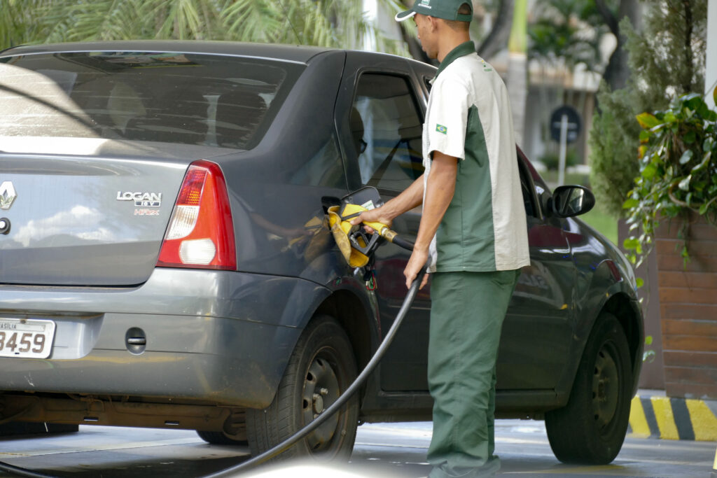 frentista com uniforme de posto que leva logo da Petrobras abastece carro logan cinza